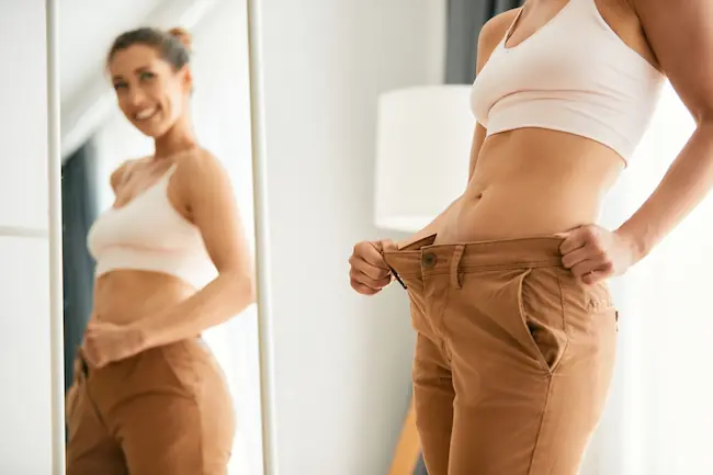 woman smiling in the mirror while admiring her smaller waistline